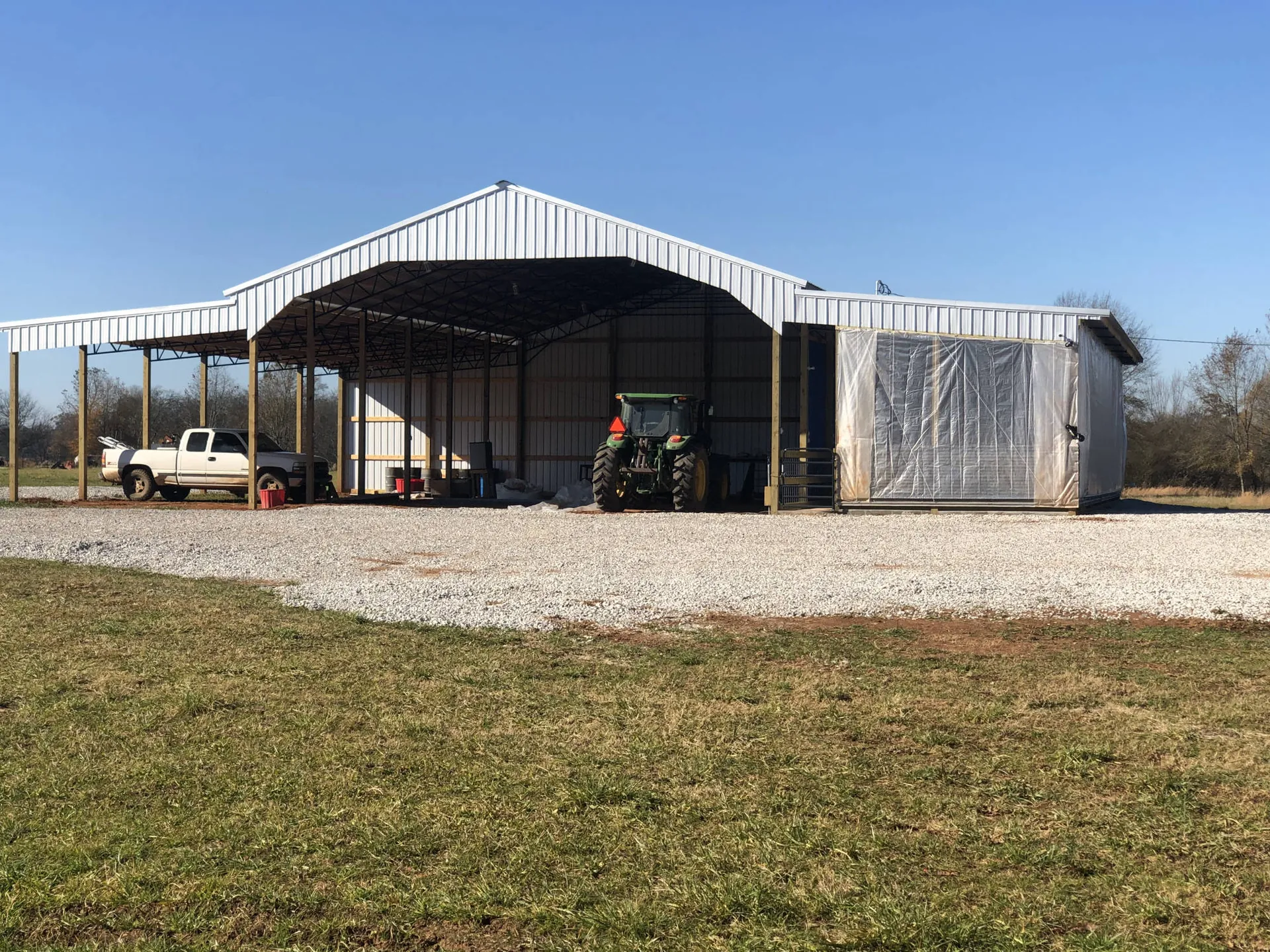 A white metal equipment shed with open bays and tractors inside