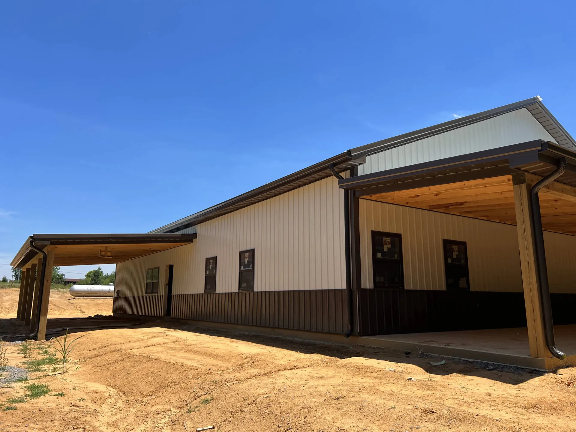 A tan and brown metal building with a deep covered side