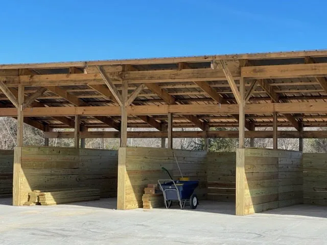 A timber-framed horse barn with a metal roof and wood stall walls