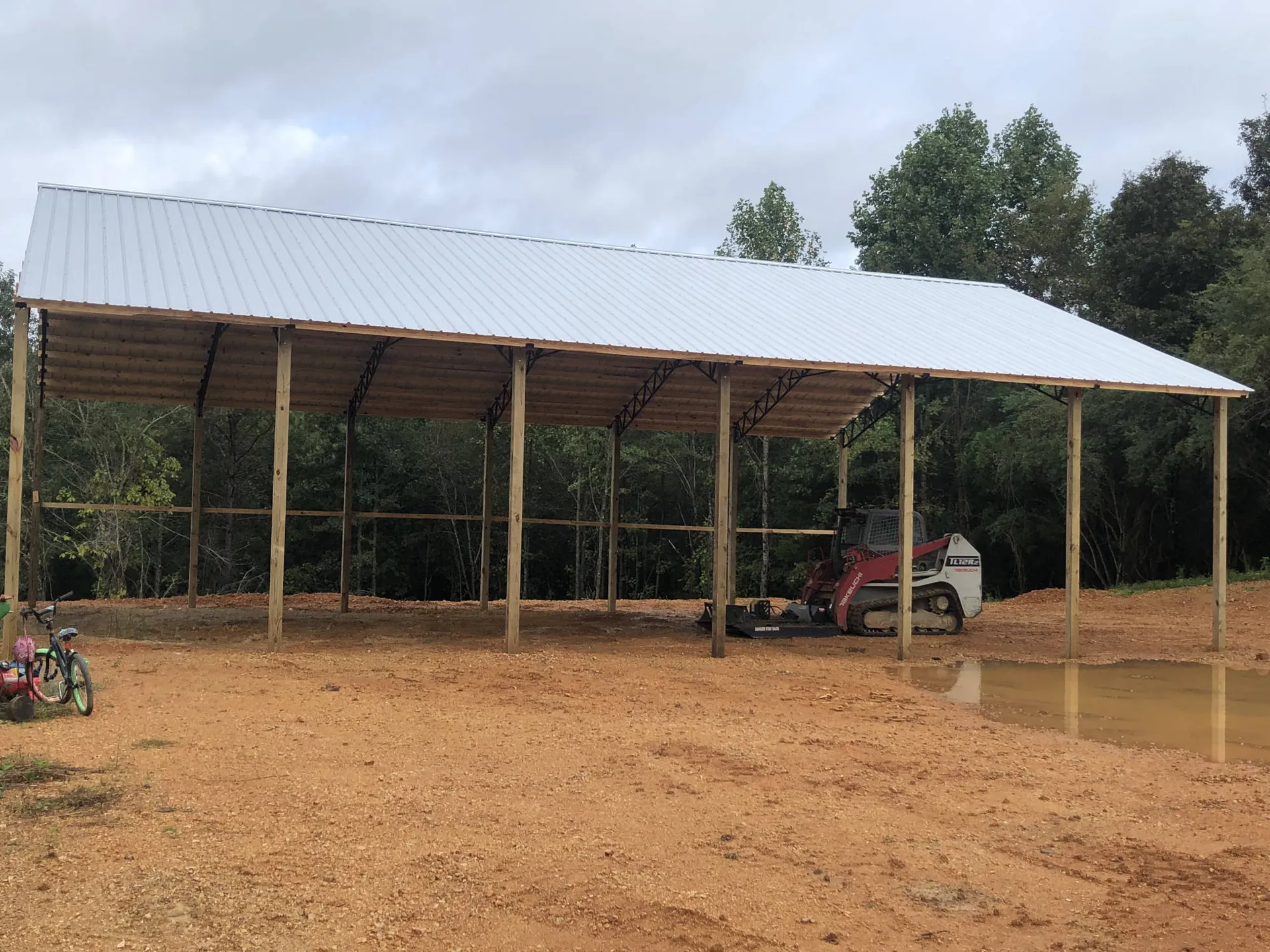 An open metal-roofed pole shelter with a tractor underneath