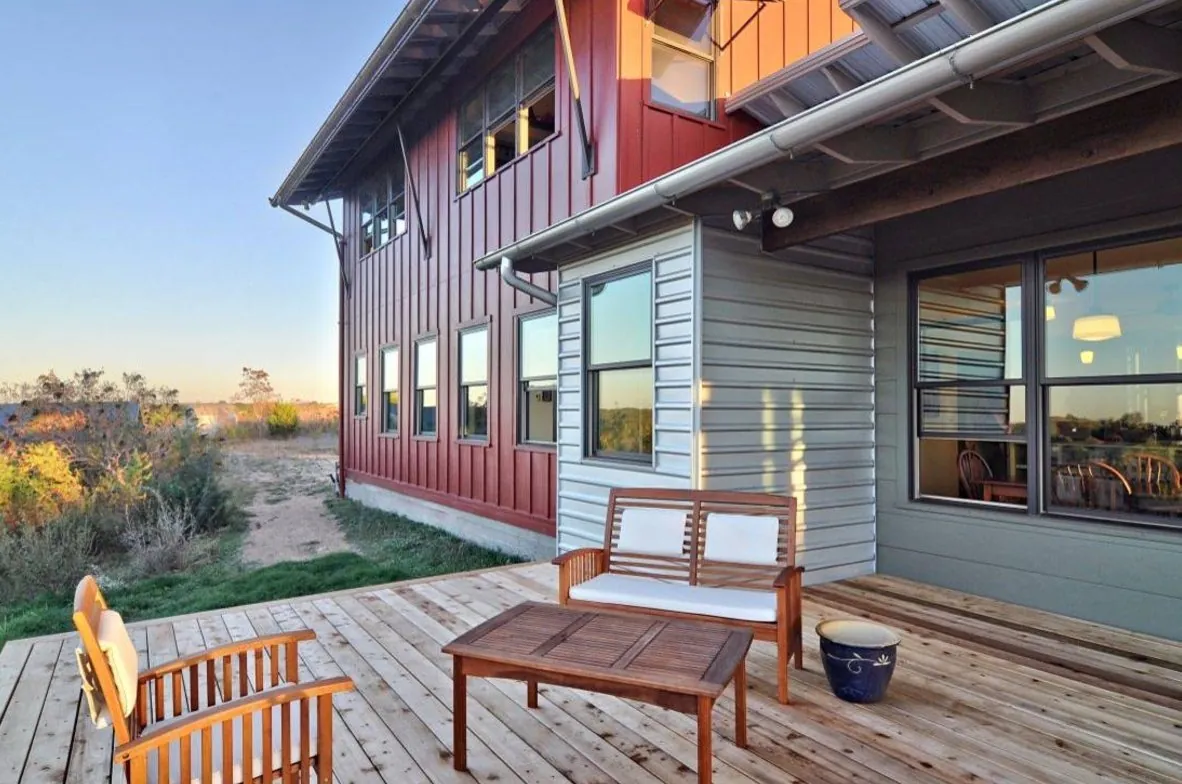 A red and gray metal home with a wooden deck and windows