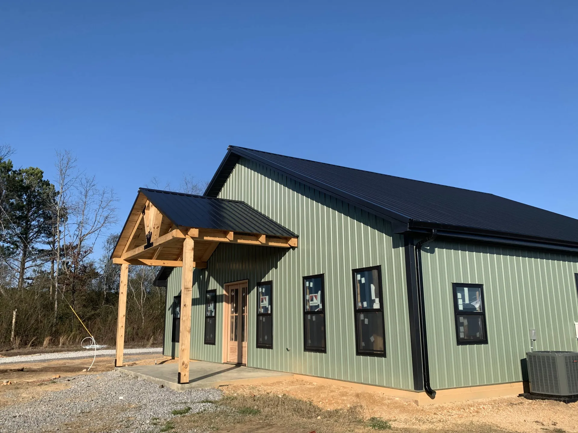 A green metal home with a black roof and timber entry porch